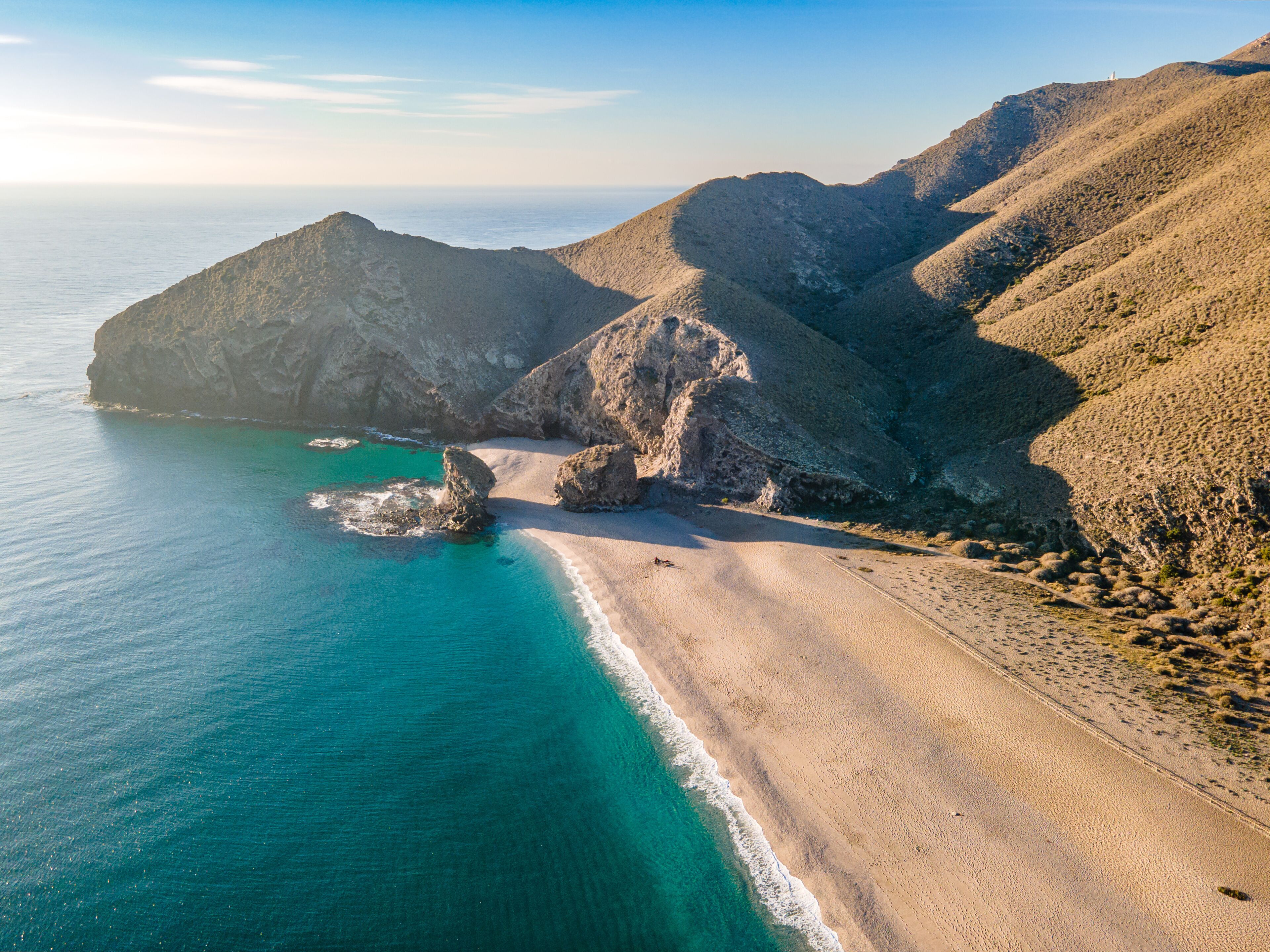 A coastal landscape with a sandy beach, rocky outcrops, and clear turquoise waters.
