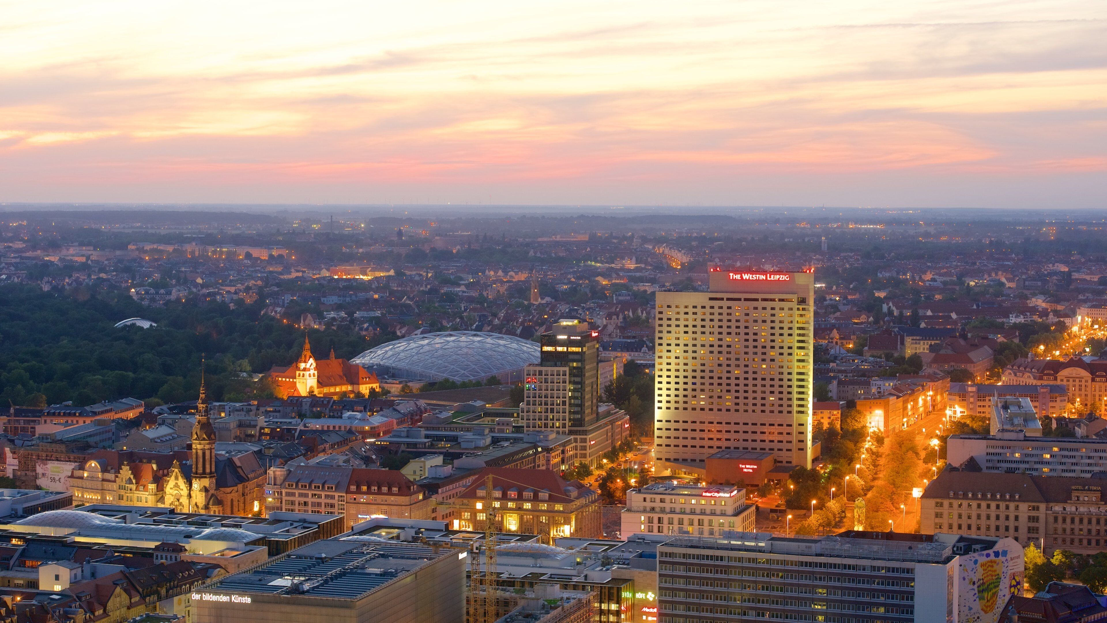 A cityscape at dusk with prominent buildings, including a tall hotel and a historic church.