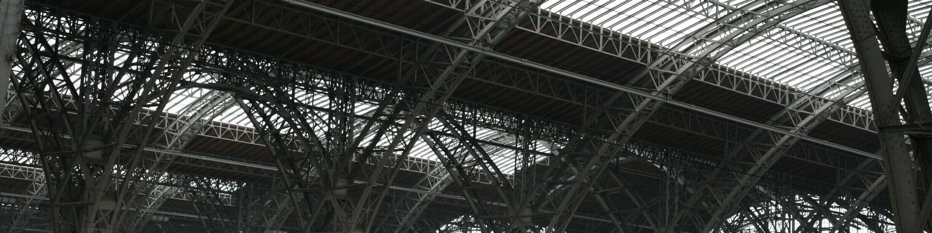 Un tren rojo y blanco en una estación con un amplio techo de vidrio y estructura metálica.