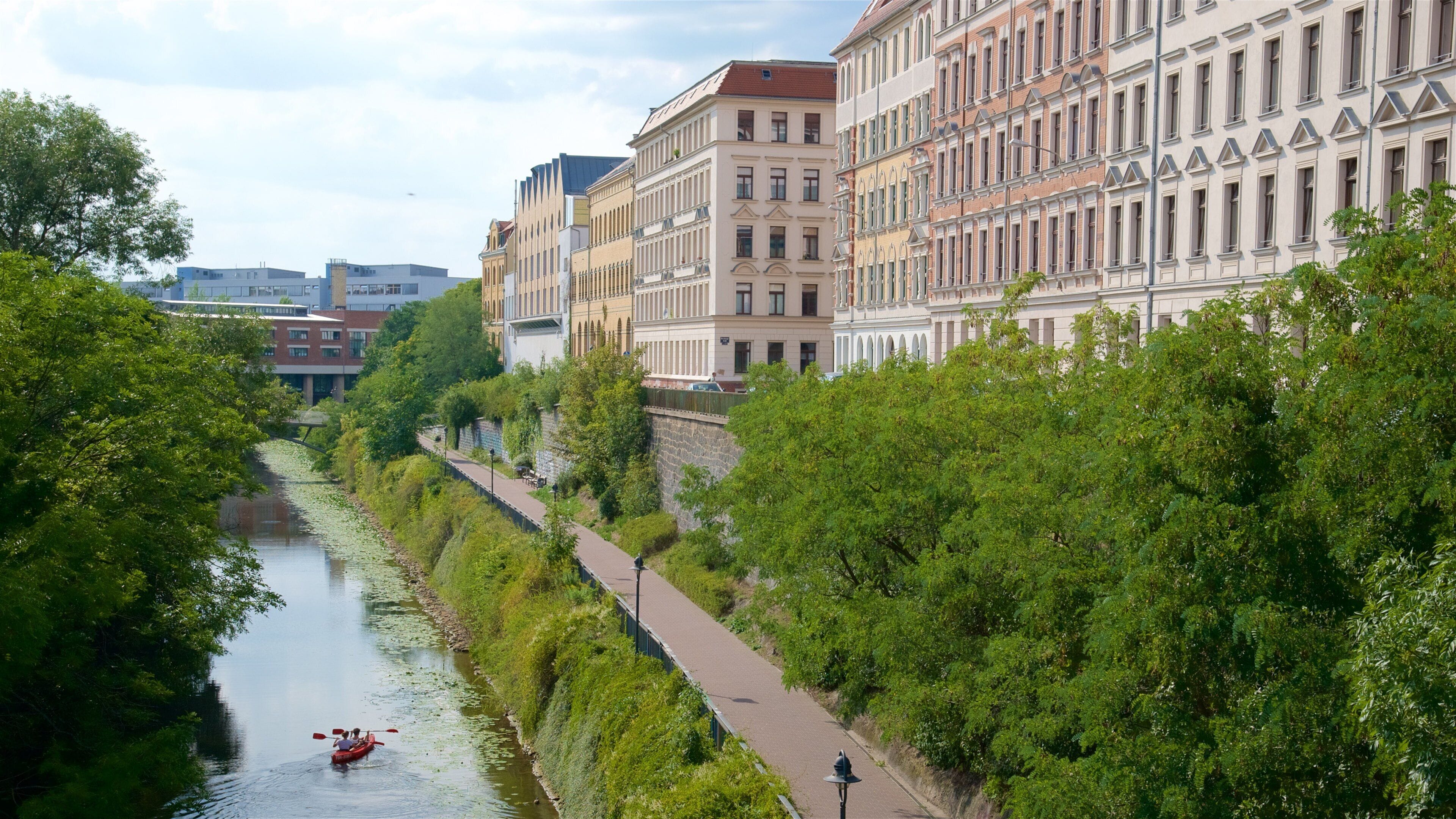 Un río con un sendero a su lado, rodeado de vegetación exuberante y edificios históricos.