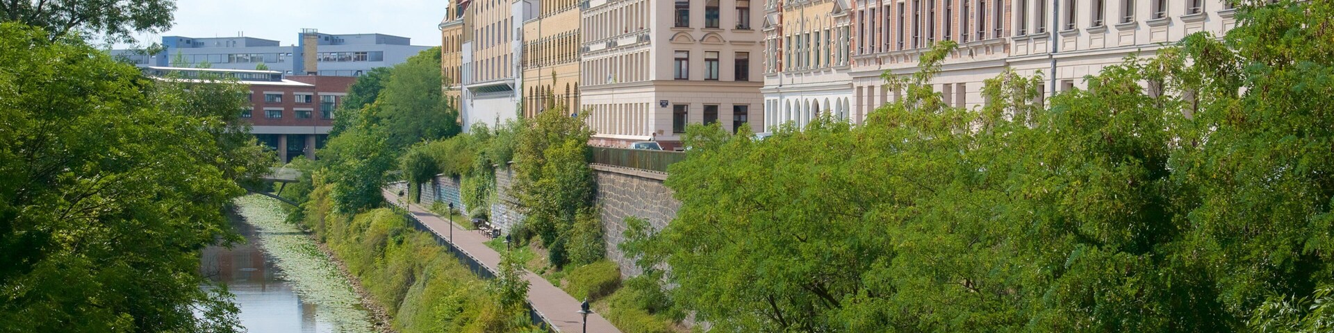 Un río con un sendero a su lado, rodeado de vegetación exuberante y edificios históricos.