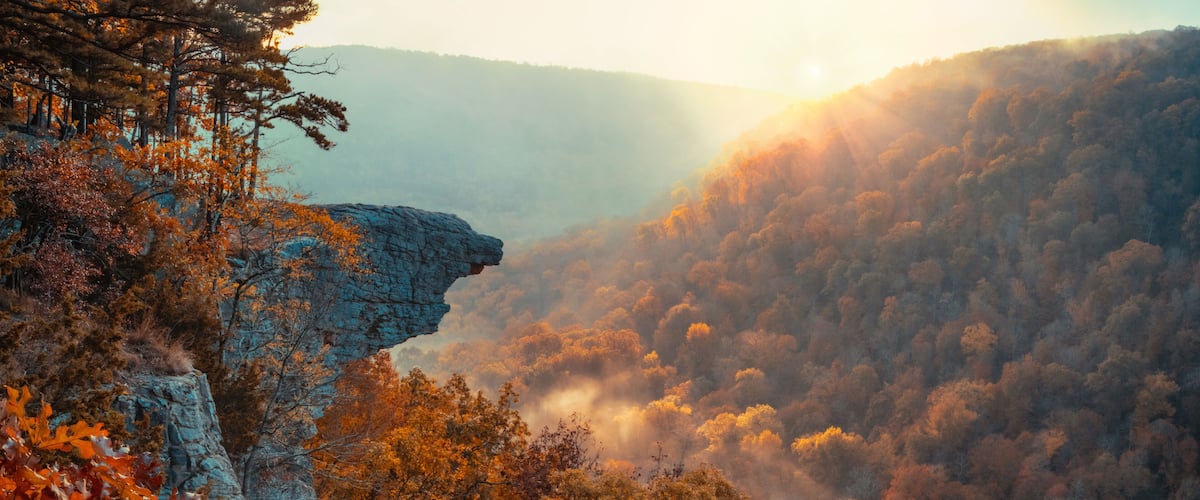 A mountainous landscape with autumn foliage and a rocky cliff.