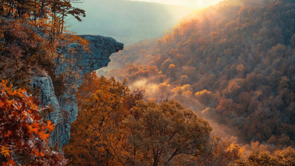 A mountainous landscape with autumn foliage and a rocky cliff.