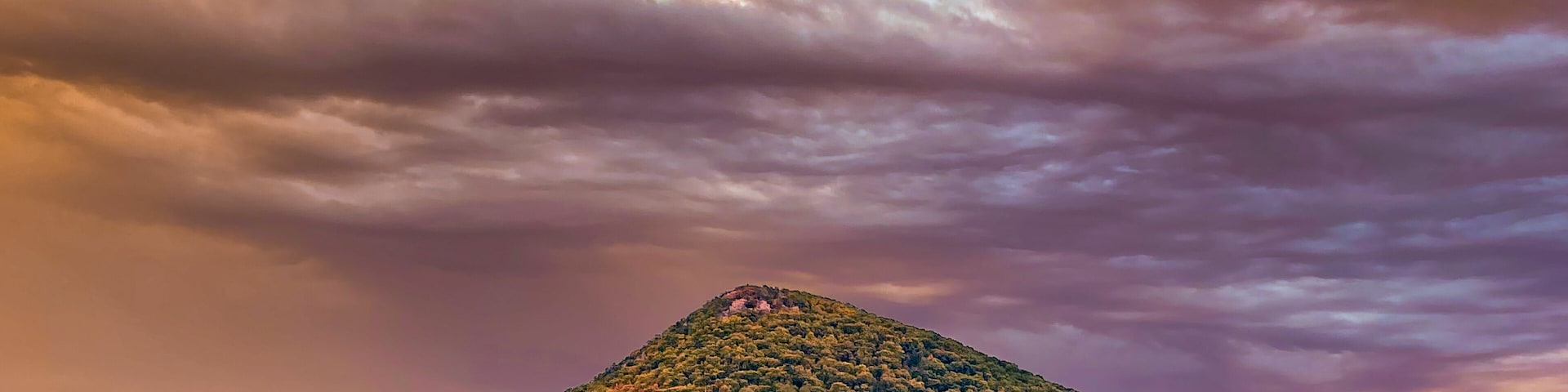 Um campo gramado com uma colina coberta por árvores de cores outonais e um céu imponente.