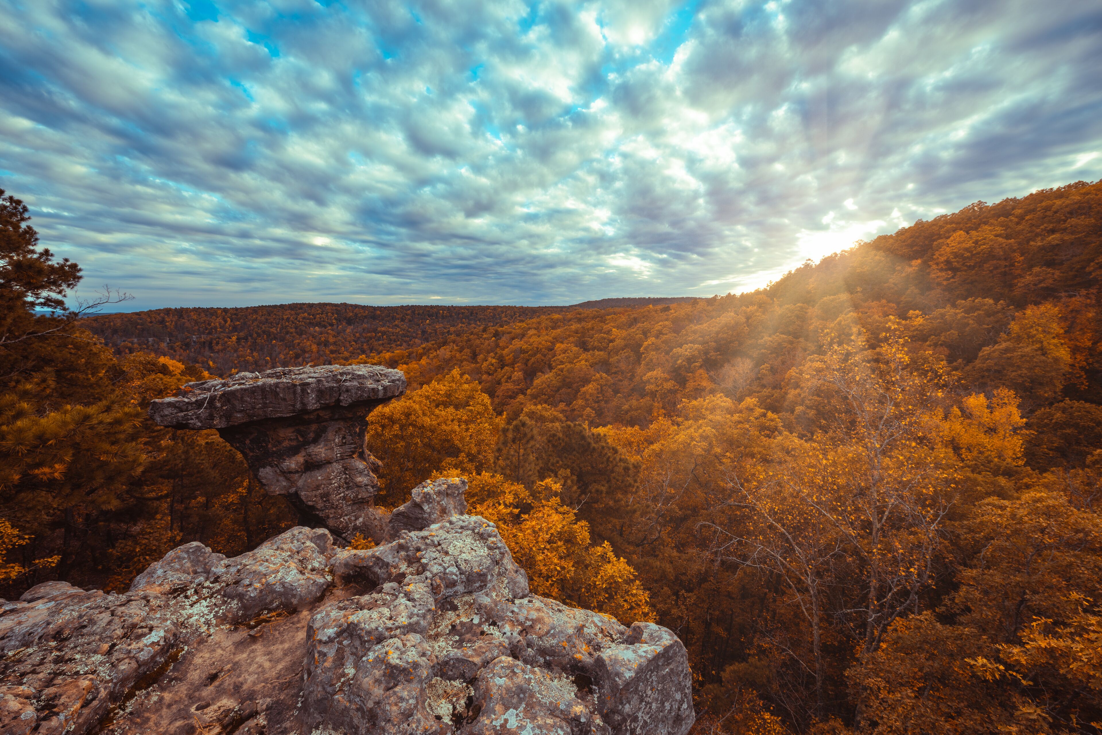 A rocky outcrop with a forested valley below under a partly cloudy sky.