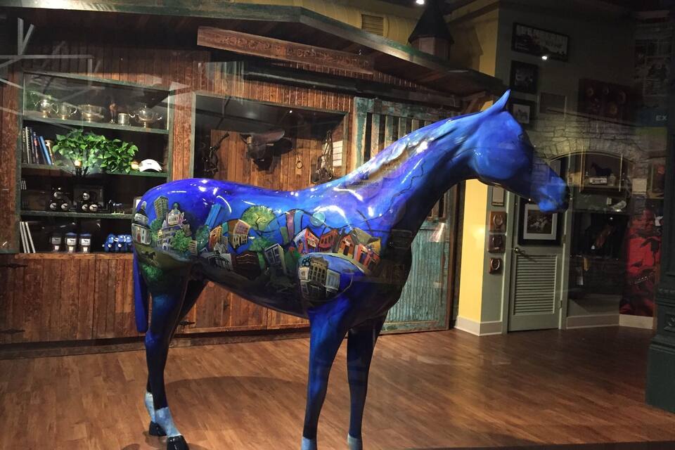 Una estatua de un caballo azul con un mural colorido en su costado.