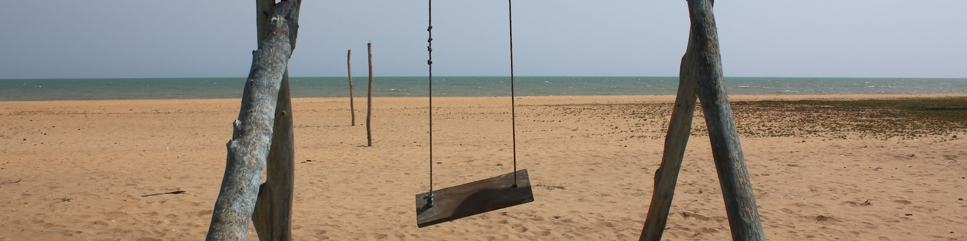 Un columpio de madera en una playa arenosa, con el océano al fondo.
