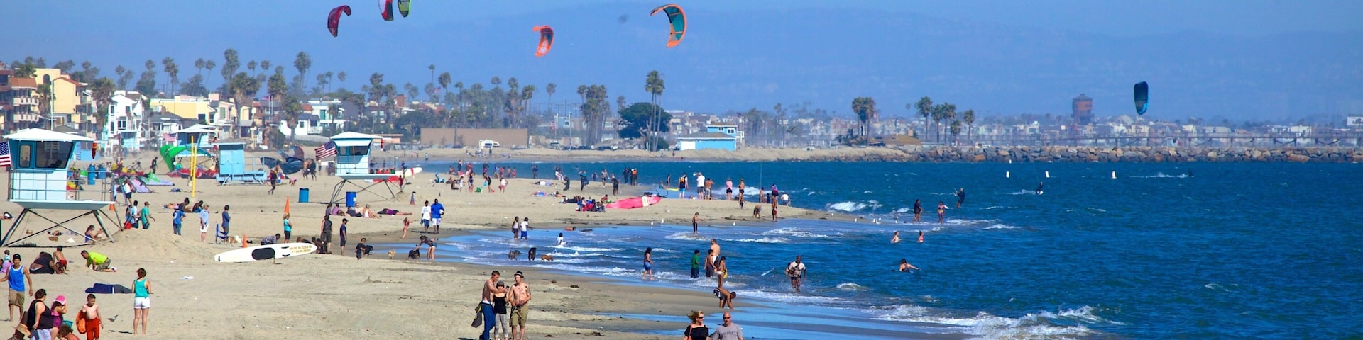 A beach with people, kites, and a lifeguard tower.