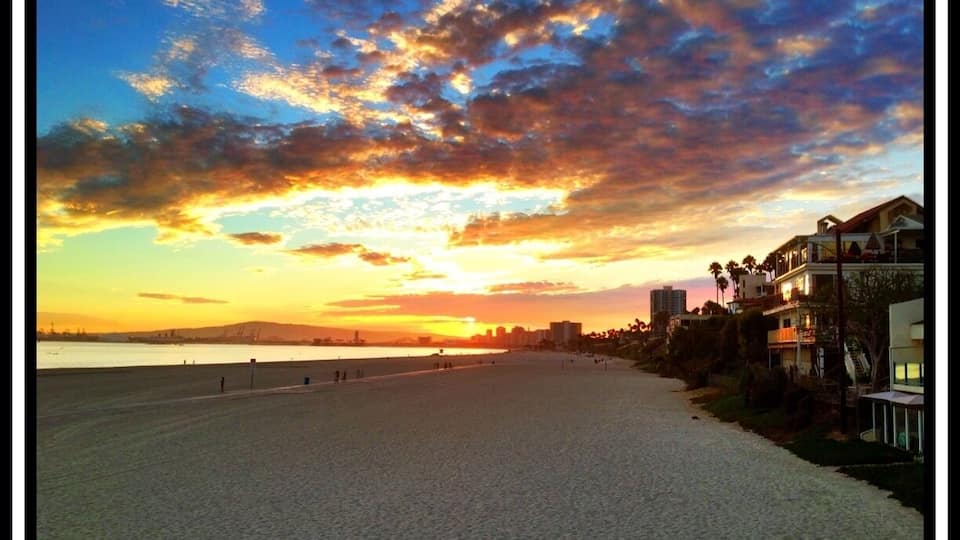Ein Strand mit Sonnenuntergang, Gebäuden und einer fernen Stadtansicht.