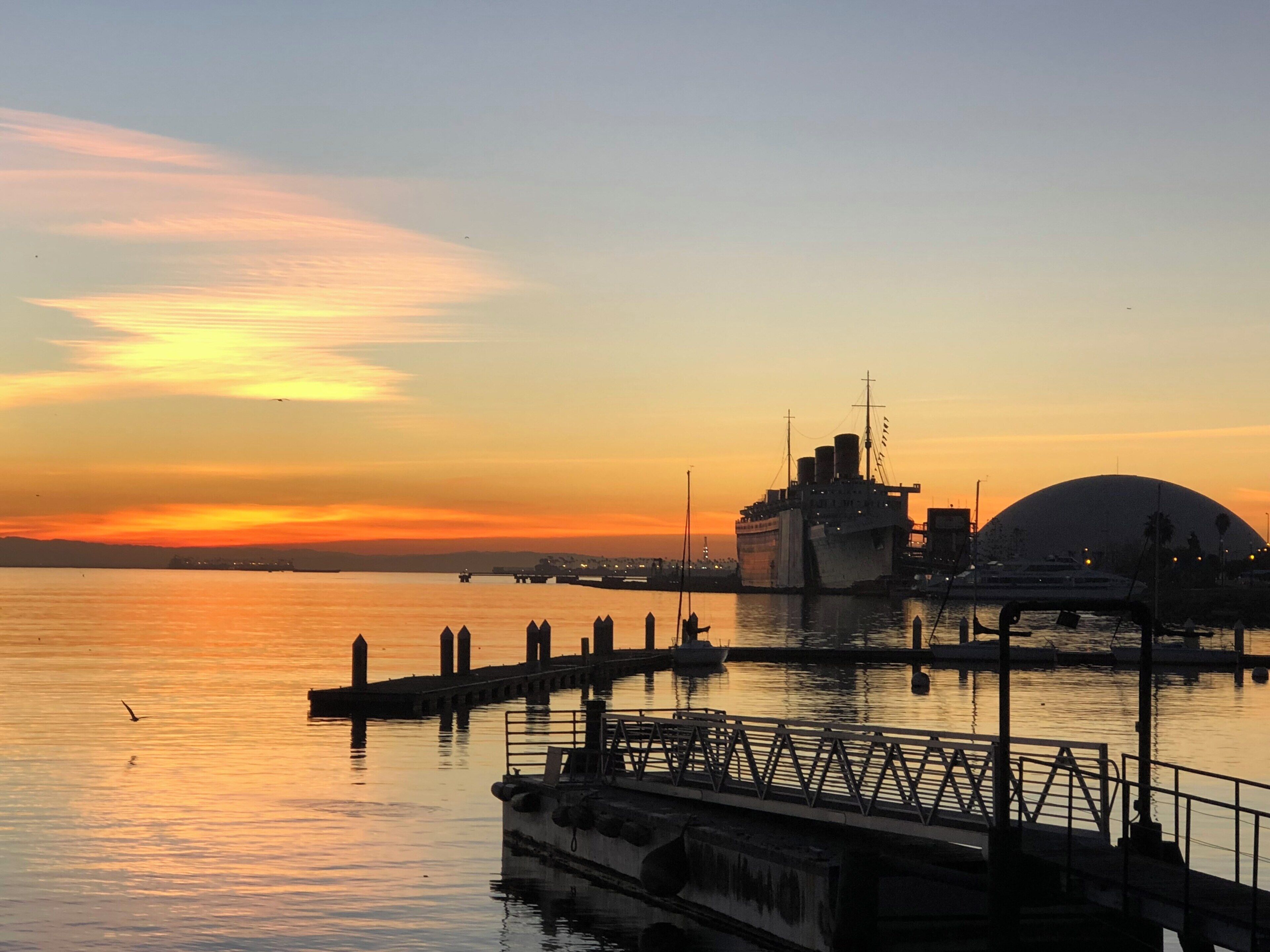 A sunset over a harbor with a large ship and a bridge.