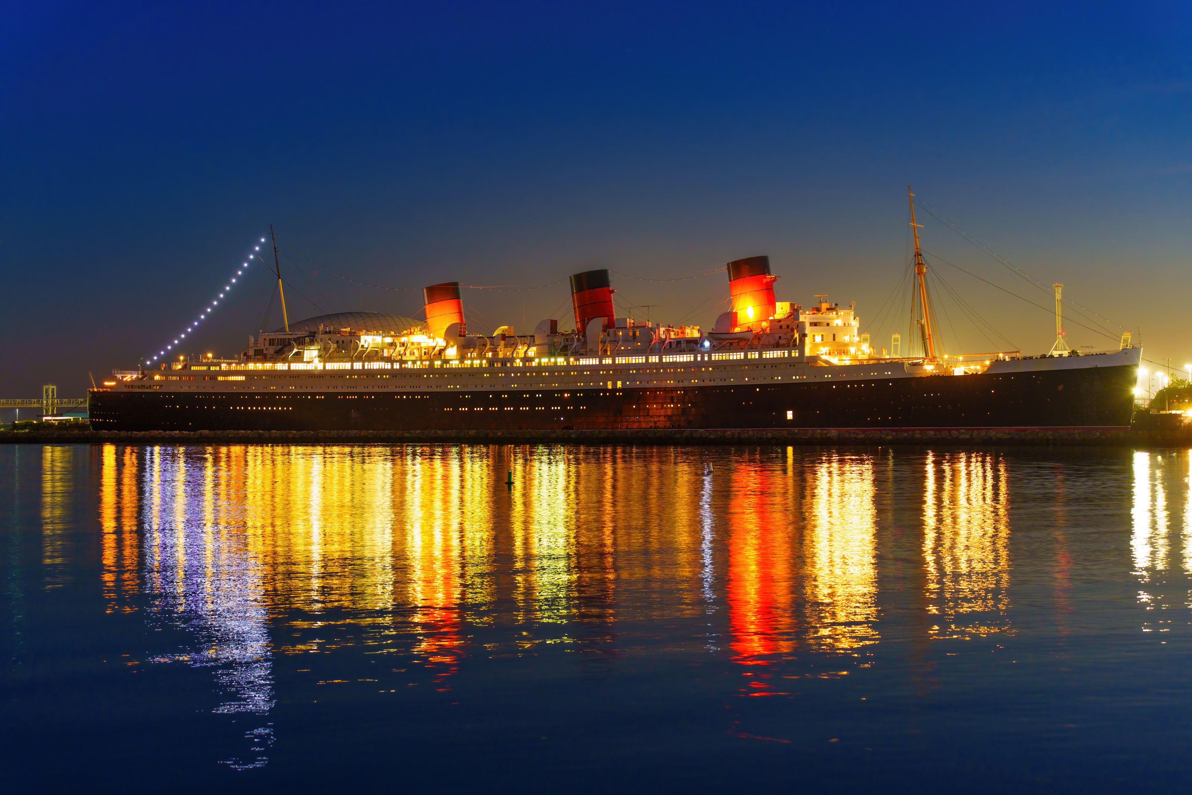 A large cruise ship at night with its lights reflecting on the water.