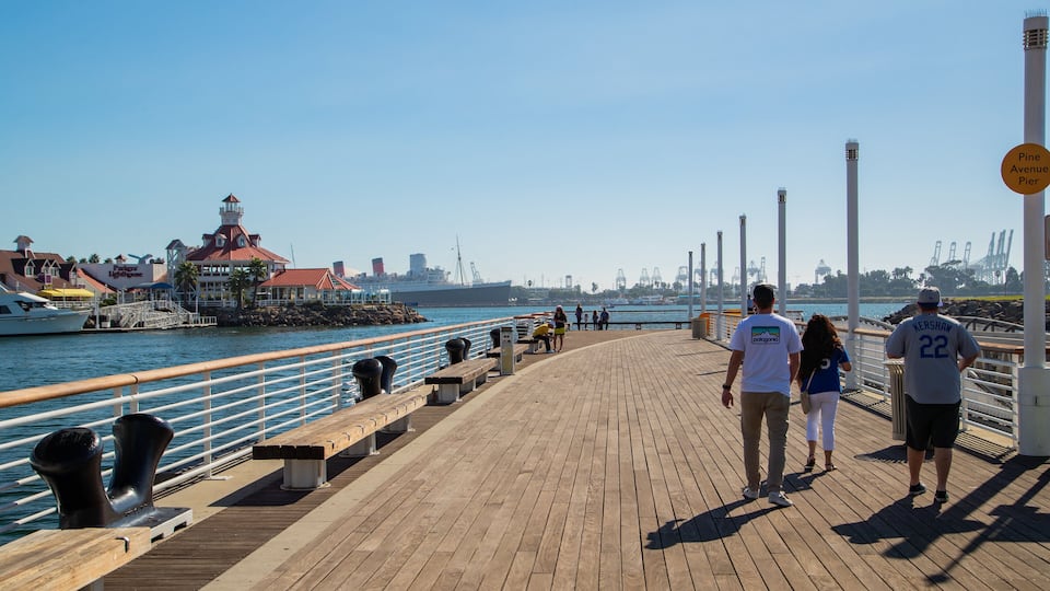 A wooden boardwalk by the water with benches, a lighthouse, and a pier with boats.