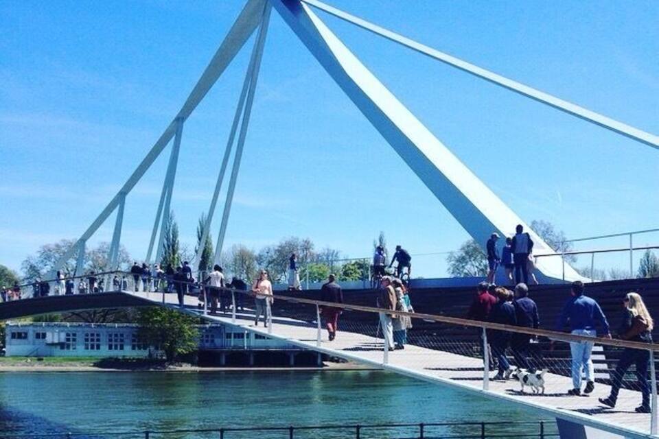 Uma ponte para pedestres sobre um rio, com pessoas caminhando e um céu azul límpido.