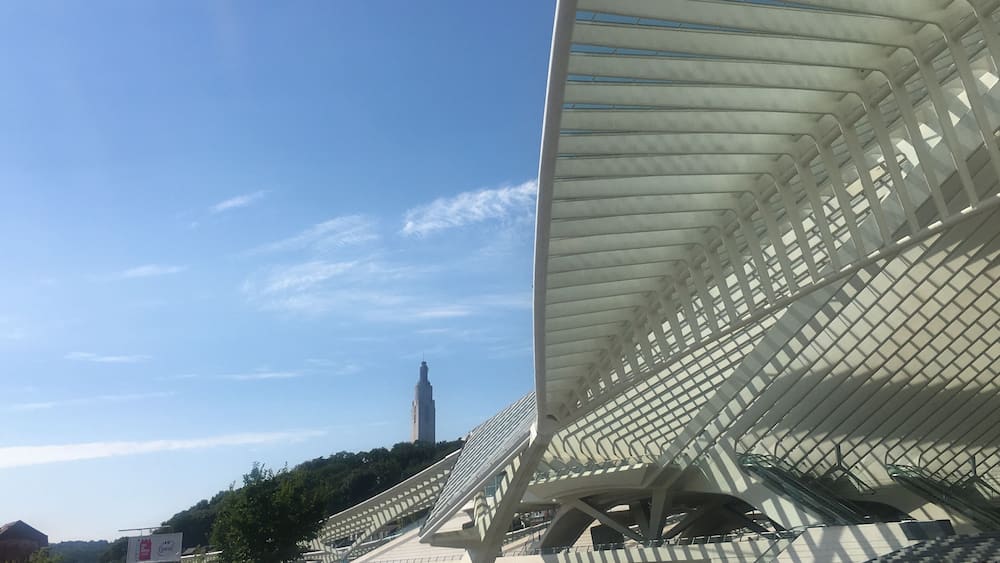Une structure architecturale moderne dotée d’un toit au design unique, d’un escalier et d’une tour visible au loin.