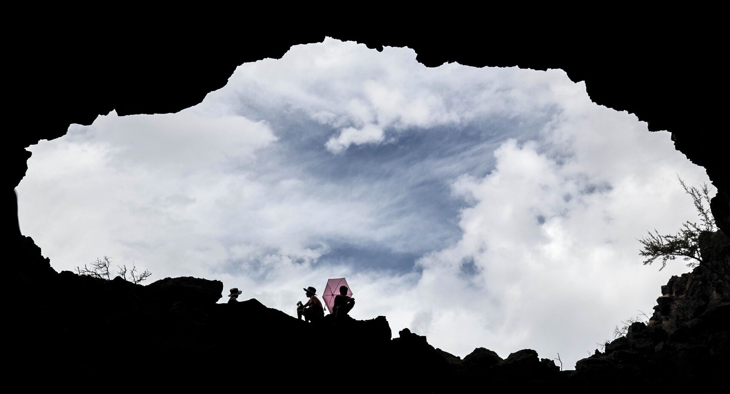Small pink sun-umbrella against a blue and white sky. This is the mouth of Heppe Cave in Lava Bed National Monument.

#lifeatexpedia