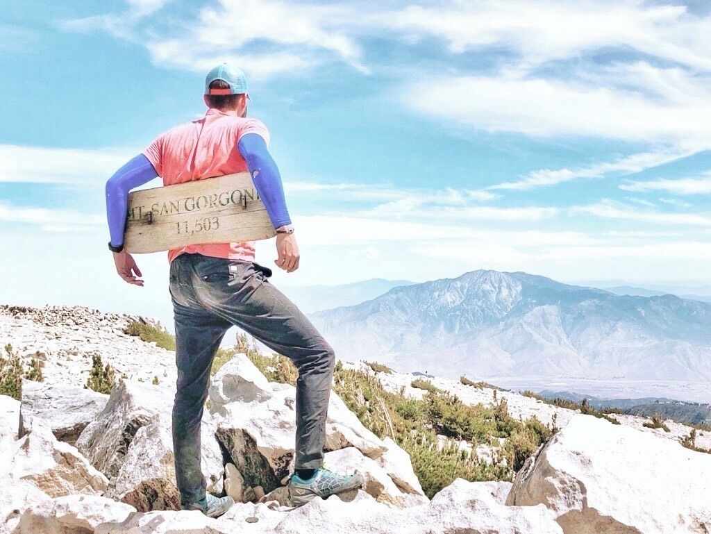 A person standing on a rocky outcrop with a sign reading "Mt. San Gorgon 11,503".