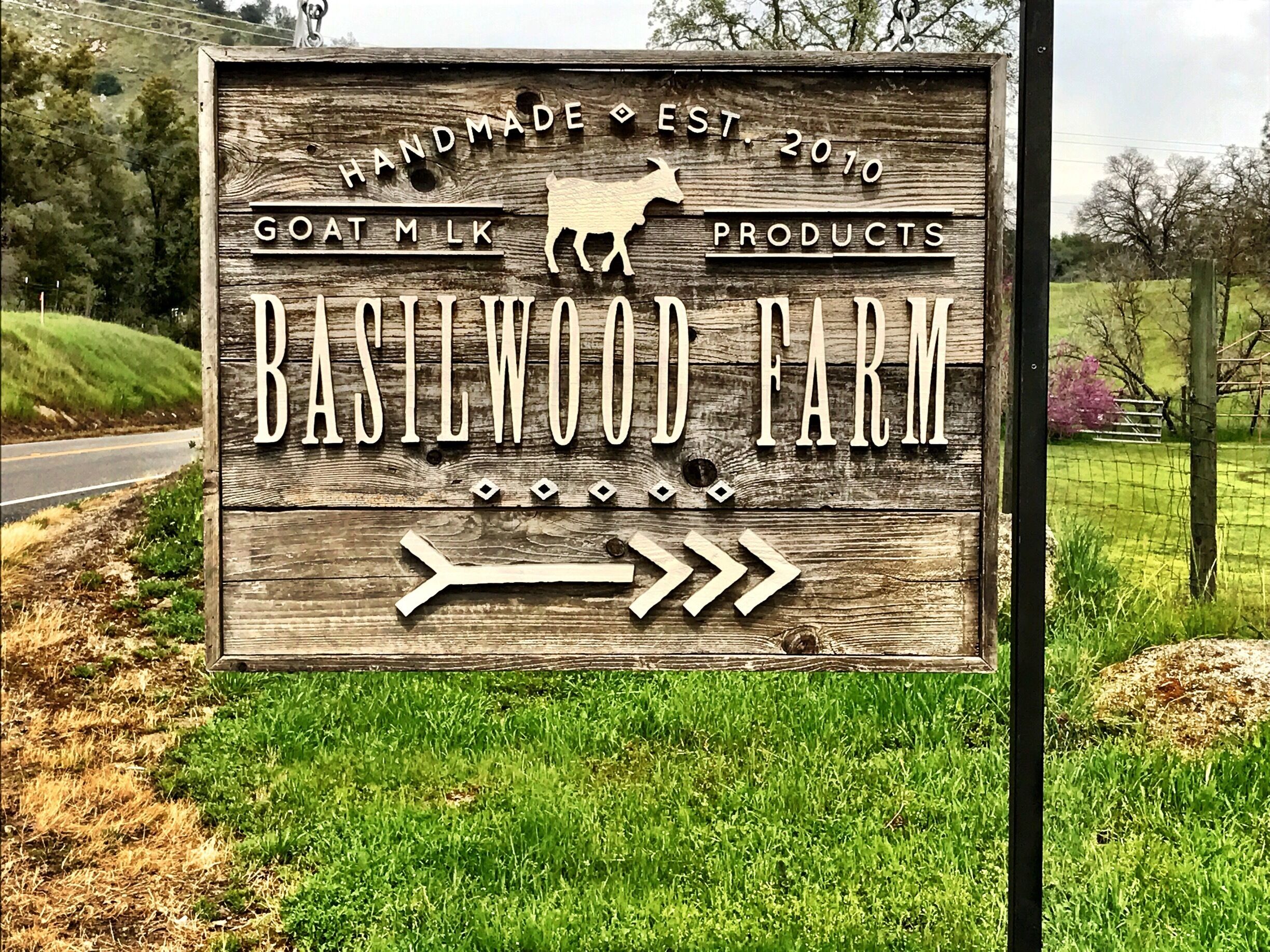 A wooden sign for Basilewood Farm advertising goat milk products.