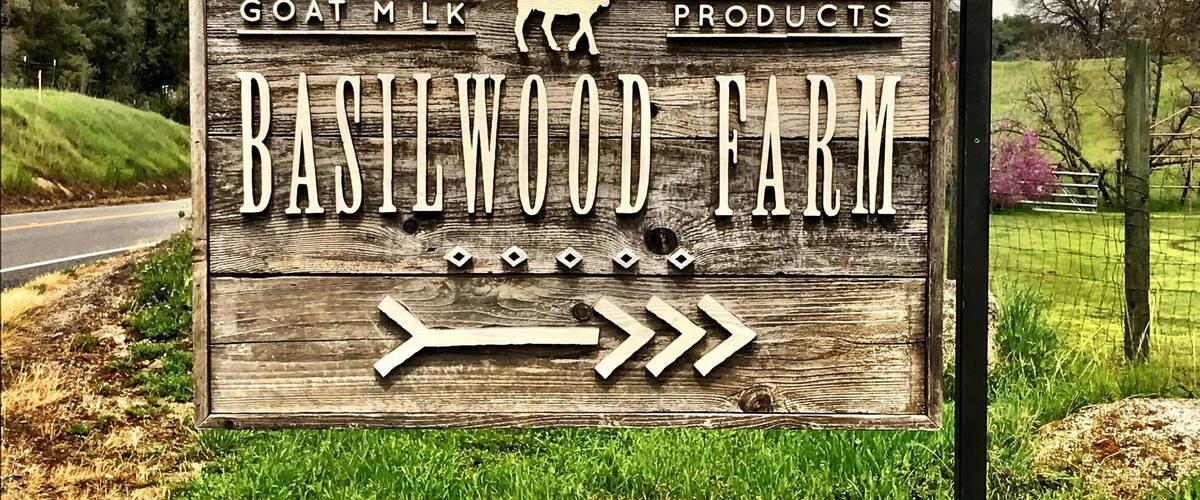 A wooden sign for Basilewood Farm advertising goat milk products.