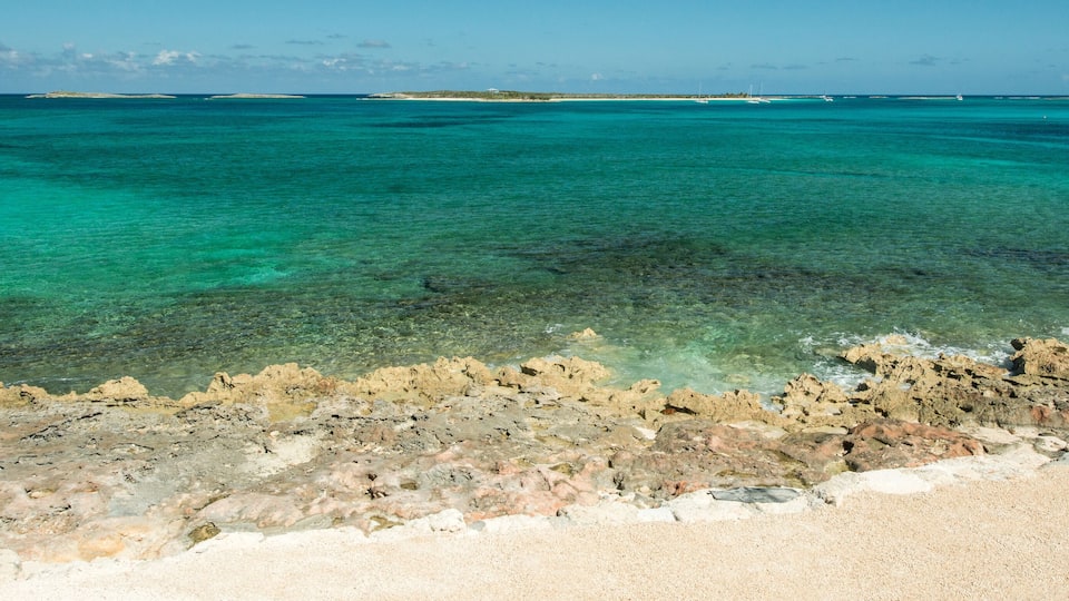 A coastal landscape with clear turquoise waters, rocky shoreline, and distant islands.