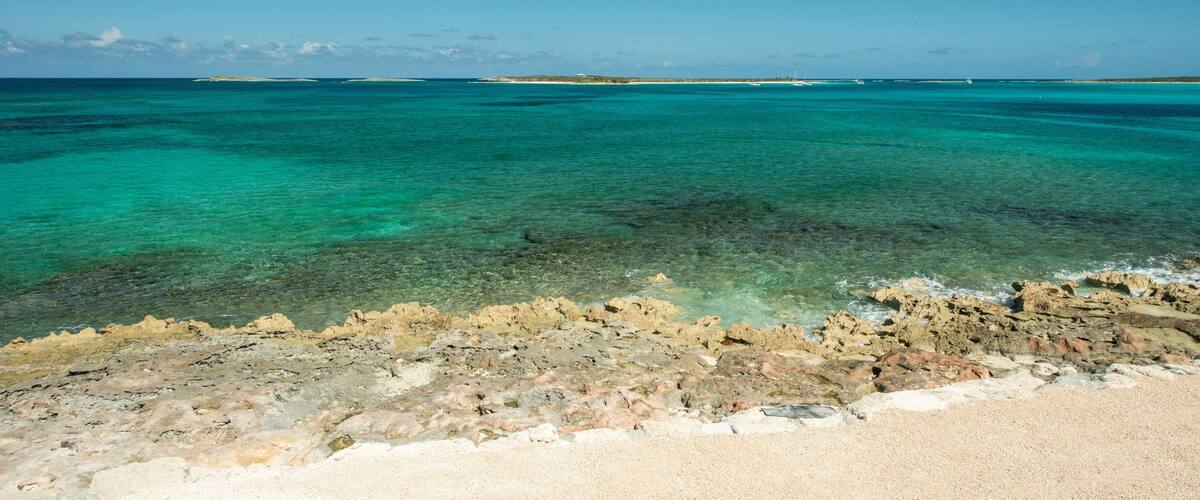 A coastal landscape with clear turquoise waters, rocky shoreline, and distant islands.