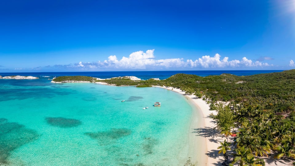 A turquoise sea, white sandy beach, and lush green hills.