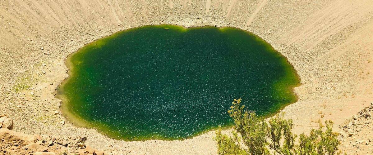 A large crater lake surrounded by a barren landscape with layered rock formations.