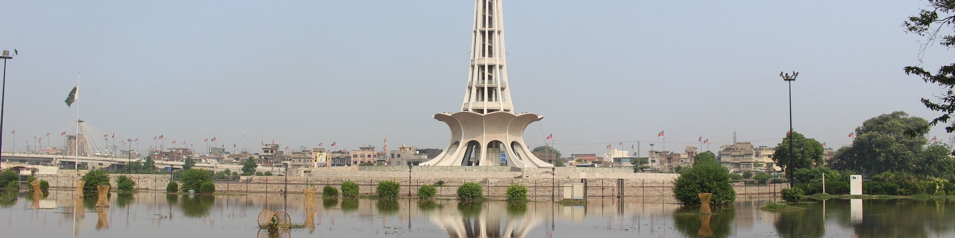 A tower with a unique design, a body of water reflecting it, and a paved walkway in the foreground.