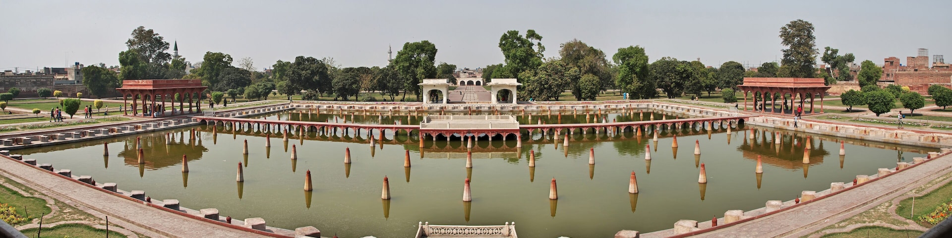 A large, rectangular water body with a central pavilion, surrounded by pathways and trees.