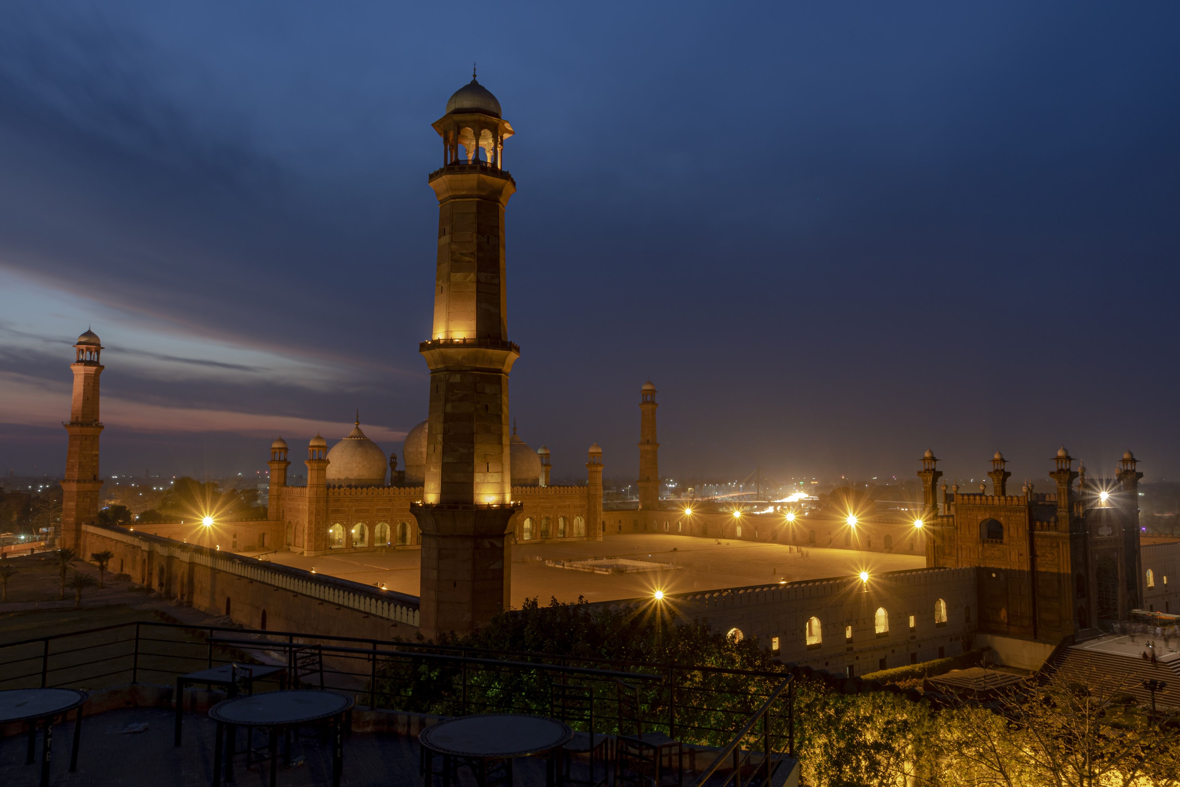 A historic mosque with a tall minaret and multiple domes, illuminated at night.