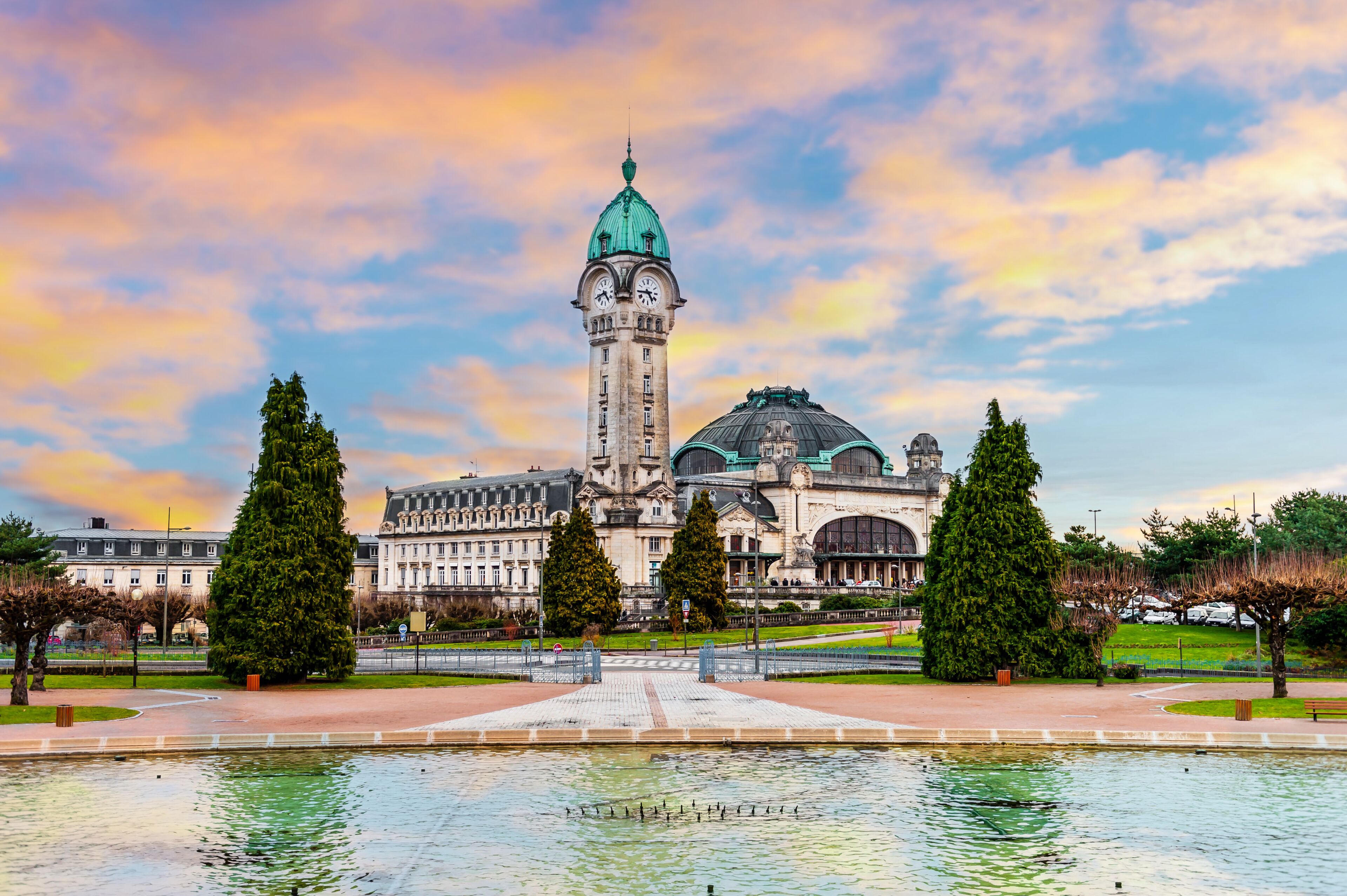 A historic building with a prominent tower and dome, surrounded by a well-maintained park with a central fountain.