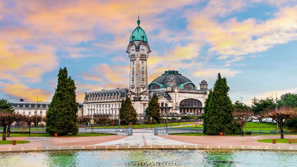 A historic building with a prominent tower and dome, surrounded by a well-maintained park with a central fountain.
