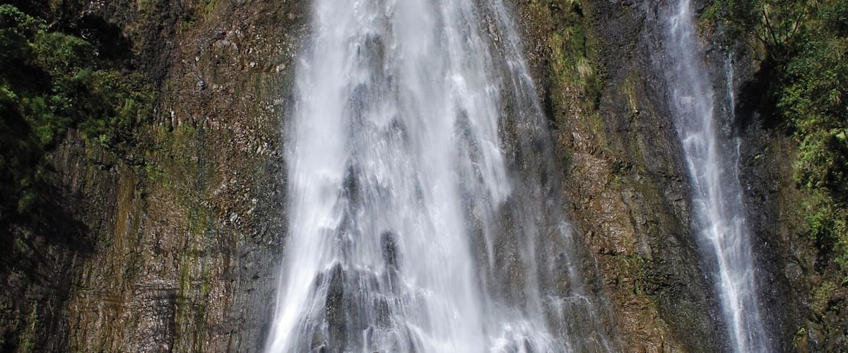 Una cascada en varios niveles que se precipita por un risco rocoso rodeado de abundante vegetación.