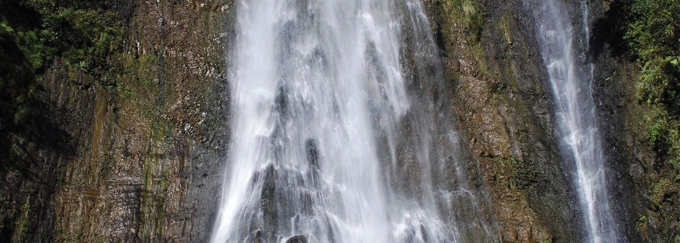 Una cascada en varios niveles que se precipita por un risco rocoso rodeado de abundante vegetación.