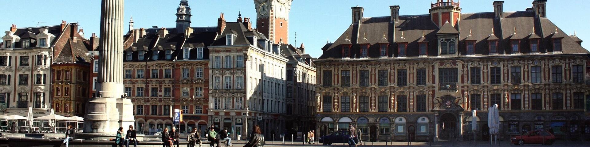 A historic square with a prominent statue, a clock tower, and ornate buildings.