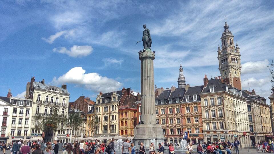 Ein belebter Platz mit einem markanten Denkmal, historischen Gebäuden und einem Glockenturm.