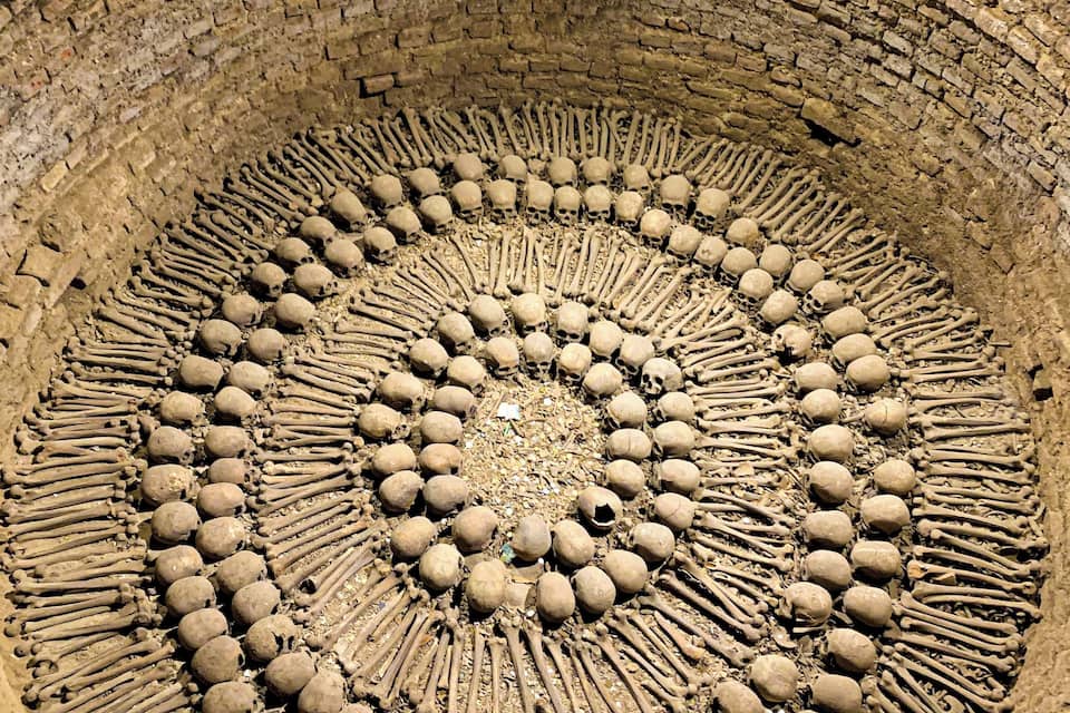 Disposición circular de calaveras y huesos dentro de una estructura de ladrillo.