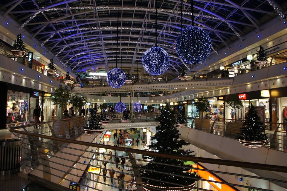 A multi-level shopping mall with Christmas decorations, including illuminated trees and hanging ornaments.