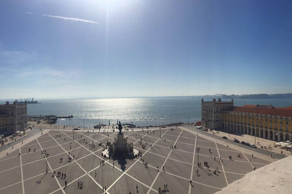 A plaza with a statue, buildings, and a view of the sea.