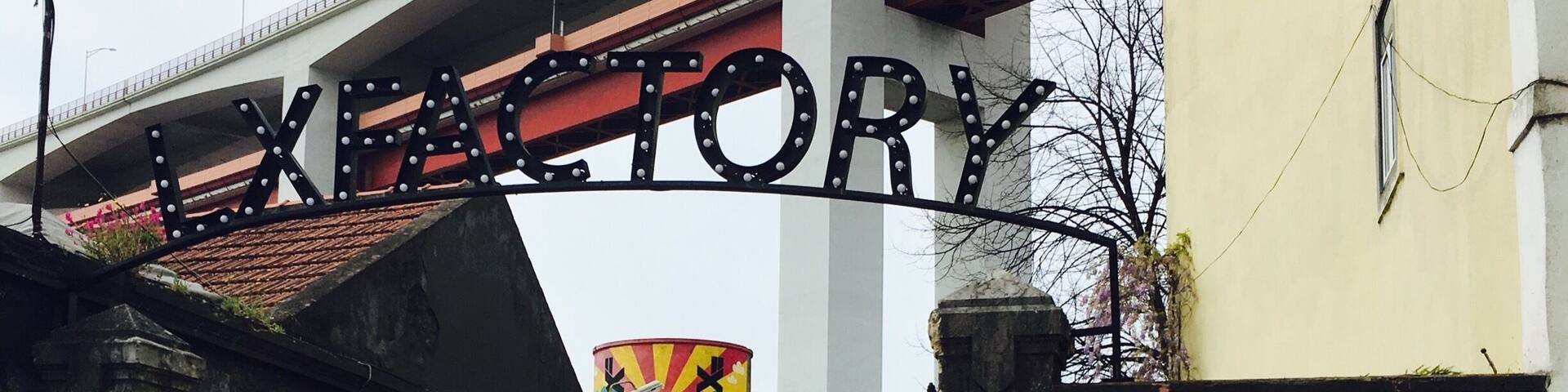 Entrada a un mercado rural con un cartel que dice 'LX RURAL DOMINGOS' y un letrero grande de 'LXFORY' arriba.