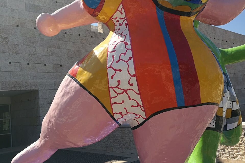 Una escultura colorida de una figura con una esfera en la cabeza, sobre un pedestal azul.