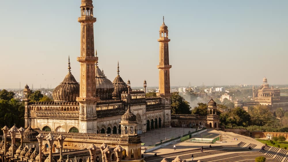 Un bâtiment historique doté de plusieurs dômes et de minarets, entouré d’une vaste cour ouverte dont le sol est pavé de motifs décoratifs.