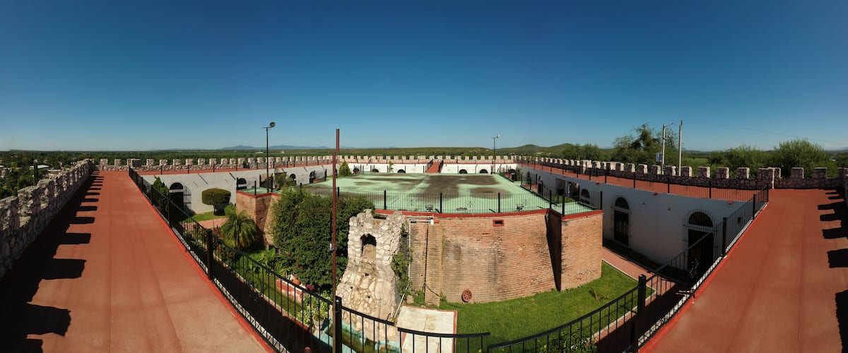 A historical fort with a central courtyard, surrounded by a red-tiled wall and a green roof.