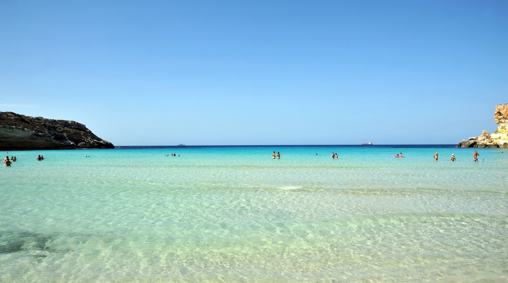 A clear turquoise sea with people swimming and sunbathing on a sandy beach.