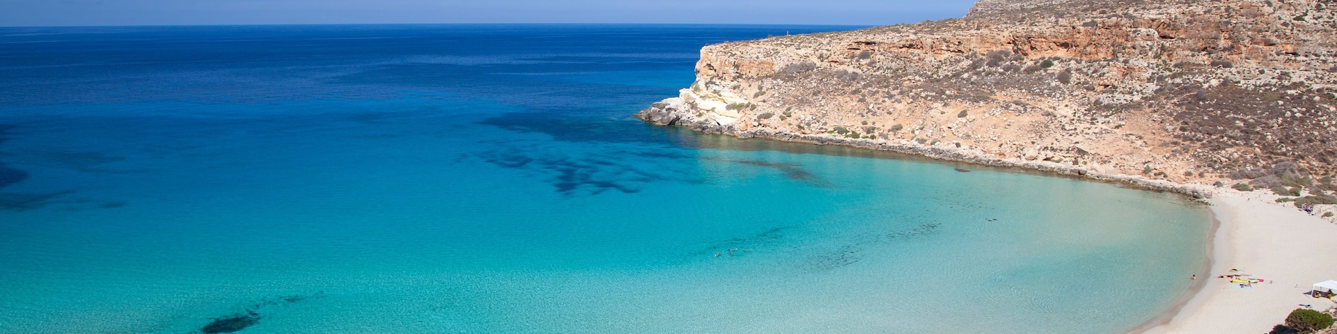 A coastal landscape with clear turquoise waters, a sandy beach, and rocky cliffs.