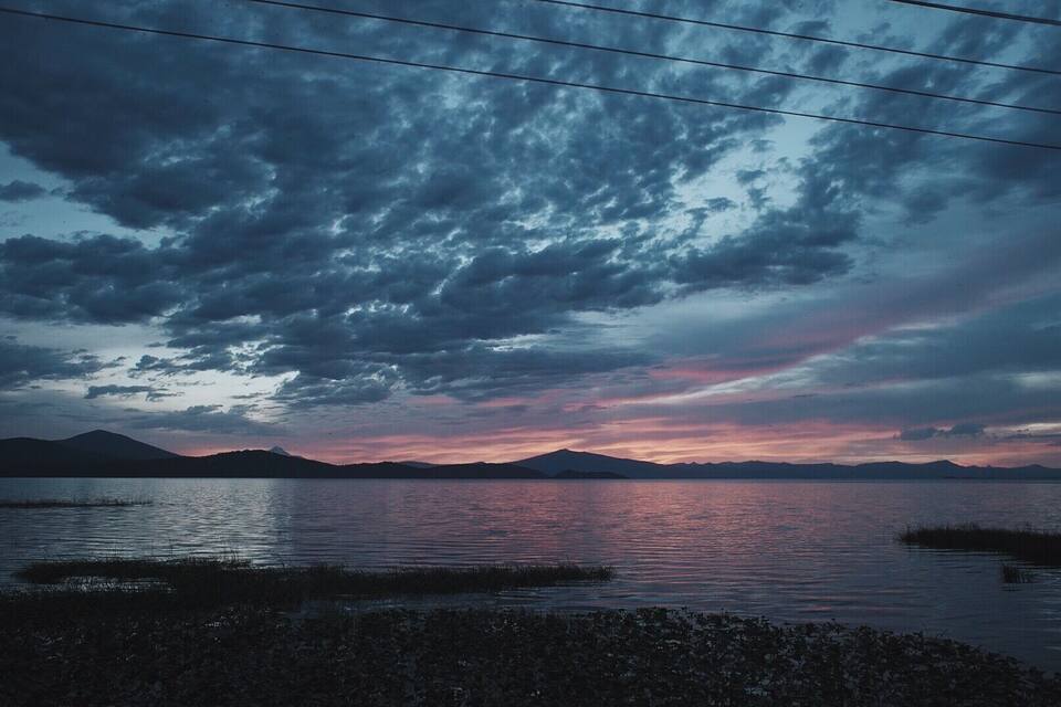 A lake with mountains in the background and a cloudy sky.