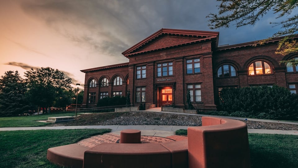 A brick building with arched windows and a sign reading "Richards Hall" at dusk.