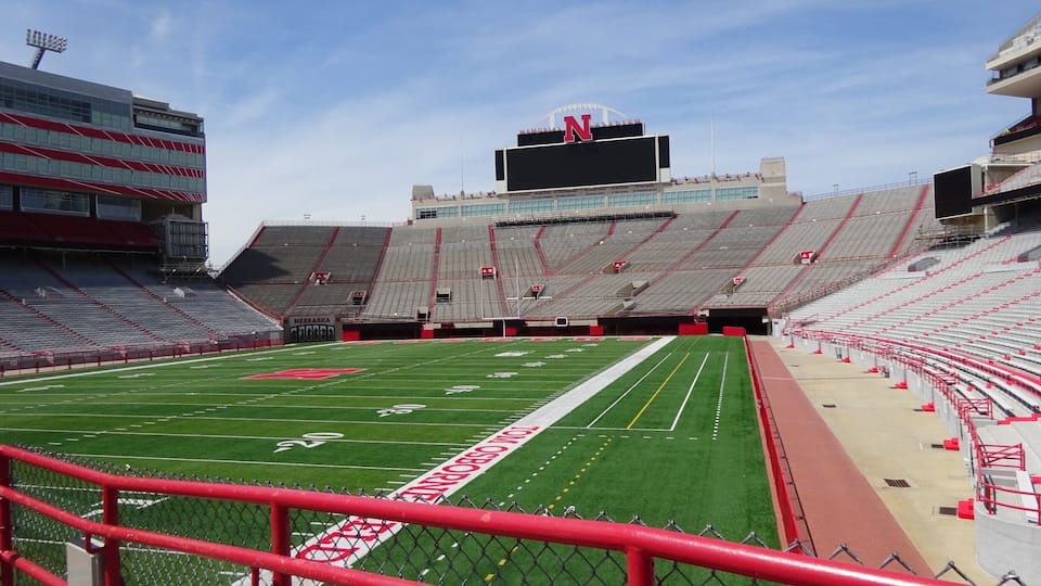 A large, empty stadium with a football field, red seating, and a scoreboard.