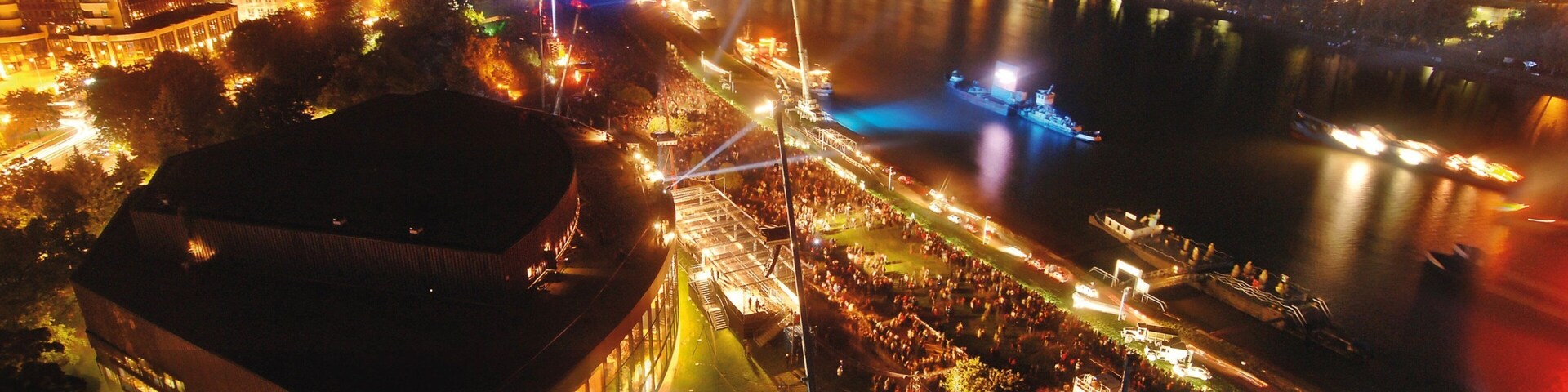 Vista noturna de uma cidade com rio, edifícios iluminados e uma ponte.