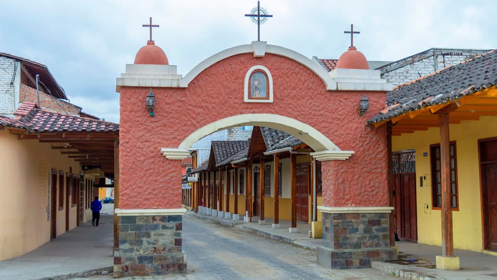 A street with a red archway, a cross on top, and a statue in the center.