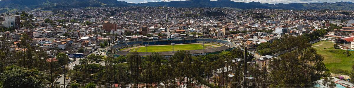 A cityscape with a large stadium surrounded by residential buildings and mountains in the background.